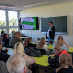 Der Schulleiter stellt in einem gefüllten Klassenraum das Schulkonzept vor